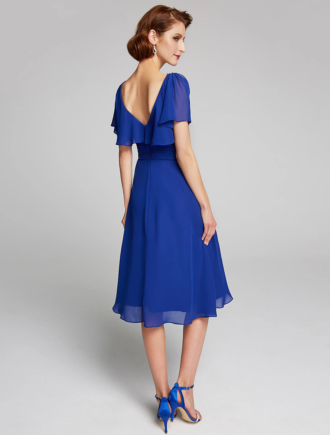 Side view of a woman in a knee-length A-line chiffon dress, showcasing the cowl neck detail.
